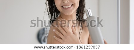 Close up cropped shot of happy positive young lady with shiny smile showering in modern bathroom. Woman holding bottle of shower product advertizing shampoo gel cream. Wide panoramic photo for banner