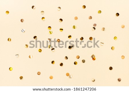 Gold confetti scattered on a beige background, top view. Color trend 2021, set sail champagne. Festive minimalistic background.