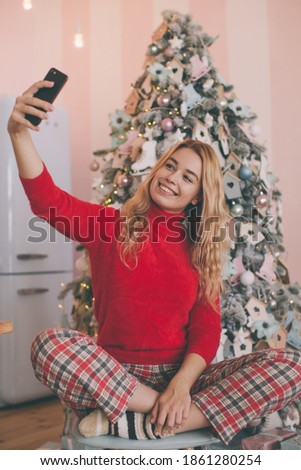 christmas concept - young woman taking selfie photo near decorated christmas tree