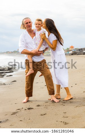 Happy family on the beach. Mother kissing daughter. Father carrying daughter in his arms. Spending quality time together. Walking barefoot. Summer holiday. Vacation in Asia. Bali island, Indonesia