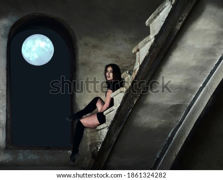 beautiful latin hispanic female dancer resting on stairway. young girl in black dress and  sitting on concrete stairs. full moon in window frame.