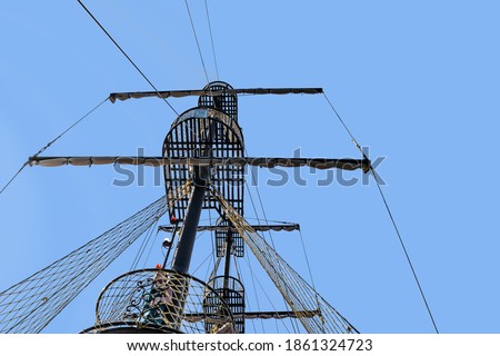 Vintage ship mast isolated on blue sky background - bottom view. Spar with sails, lookouts and navigation lights, close-up