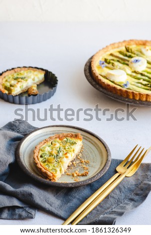 A small asparagus egg tart on a plate, cut in half with golden crumbs. Gold cutlery and dark grey napkin complete the informal table setting. White space at the top for copy text.