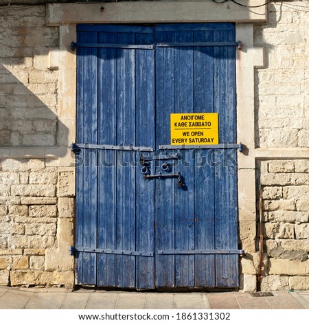 An old blue wooden exterior door in a natural stone wall in Limassol Old Town, Cyprus, with a bilingual notice in Greek and in English.