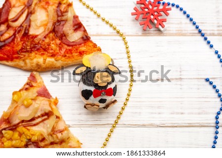 New Year's figure of a bull and a piece of pizza on a white wooden background.