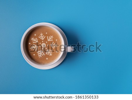 A Cup of coffee with milk in a blue mug on a blue background, and the silhouette of a Christmas tree on the foam, flat lay, copy space. Christmas concept.