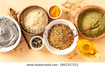 Ingredients for homemade skin and hair care in bowls top view. Henna powder, dry chamomile, turmeric, cosmetic clay, and oil. Ayurvedic skin care products.