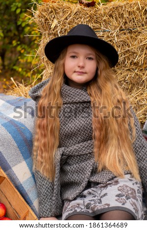 cute brunette teen girl in black hat and gray coat near autumn elements decoration - pumpkins, plaid, hay. Cosiness, autumn. 