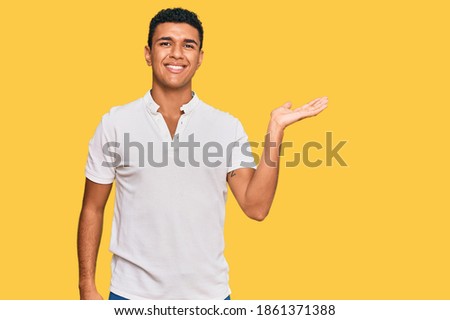 Young arab man wearing casual clothes smiling cheerful presenting and pointing with palm of hand looking at the camera. 