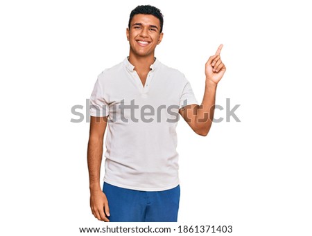 Young arab man wearing casual clothes with a big smile on face, pointing with hand finger to the side looking at the camera. 