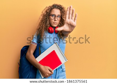 Beautiful caucasian teenager girl wearing student backpack and holding books with open hand doing stop sign with serious and confident expression, defense gesture 