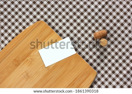mockup, scene creator. one empty business card, wine corks and a bamboo cutting Board on a checkered tablecloth, top view. kitchen, table. copy space.