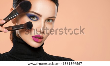 Portrait of a girl with cosmetic brush near face. Woman making makeup on the face using makeup brush. One half face of a beautiful white woman with  bright makeup and the other is natural.  Royalty-Free Stock Photo #1861399567