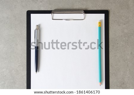 Template of white paper with a ballpoint pen and simple pencil on light grey concrete background in a black tablet with a clip. Concept of new idea, business plan and strategy, development and