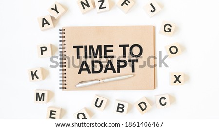 Text TIME TO ADAPT on the craft colored notepad with block wood cubes on the white background Royalty-Free Stock Photo #1861406467