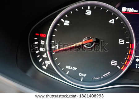 Rev counter of car selective focus closeup with copyspace.Tachometer or revolution counter, RPM gauge with red glowing needle on car dashboard with fuel and engine temperature indicators. Royalty-Free Stock Photo #1861408993