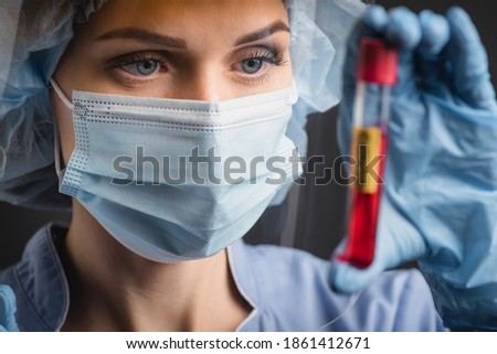 nurse in medical mask holding test tube on blurred foreground isolated on dark grey