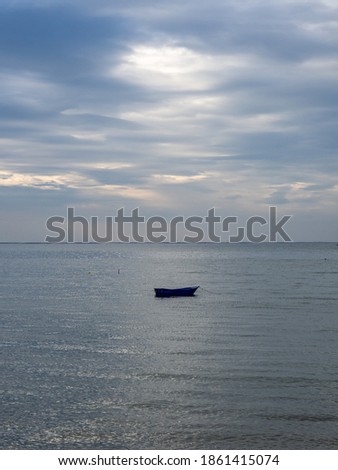 A lonely boat floating in the sea on a cloudy day with the blue sky and light through the cloud in the background. Use for wallpaper, backdrop, print in the concept of loneliness, peaceful, calmness.