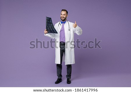 Full length of funny bearded doctor man in medical gown hold x-ray brain by radiographic image ct scan mri showing thumb up isolated on violet background. Healthcare personnel health medicine concept Royalty-Free Stock Photo #1861417996