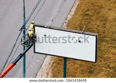 Workers hang a roadside poster on a billboard near a road