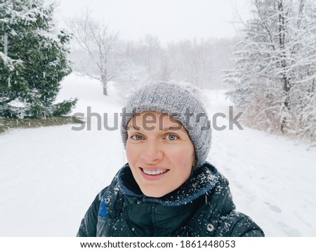 Happy smiling Caucasian woman taking selfie photo on smartphone in park outdoor on winter day.  Heavy snowfall and snowstorm. First frost snow. Beauty in nature landscape.