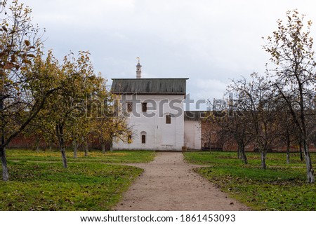 Landscape of an old white brick house in an apple garden behind a large old brick fence. Autumn cloudy day
