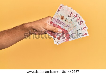 Hand of hispanic man holding colombian 10 pesos banknotes over isolated yellow background.