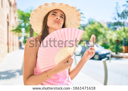 Young hispanic woman on vacation wearing summer style using hand fan at street of city