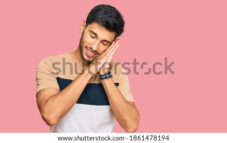 Young handsome man wearing casual clothes sleeping tired dreaming and posing with hands together while smiling with closed eyes. 