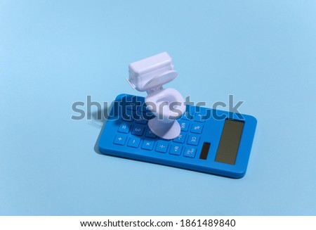 Mini white toilet and calculator on blue background with deep shadow. Minimalism.