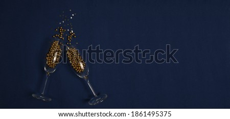 Two champagne glasses with gold balls and stars on a dark blue background. Happy holiday concept. Top view with place for text.