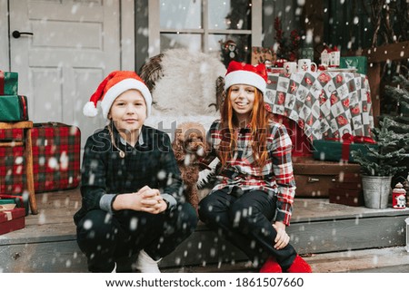 Children a boy and a girl in Santa hats with a dog have fun and enjoy the first snow on backyard porch of a house decorated for Christmas and New Year, soft focus 