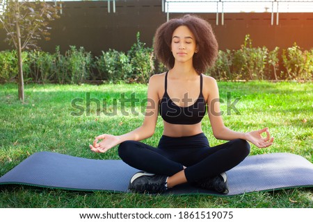 Charming African-American girl with dark hair is calm and relaxed in the lotus pose, doing meditation. Glare in the photo in upper right corner. People, zen, sports and freedom concept.
