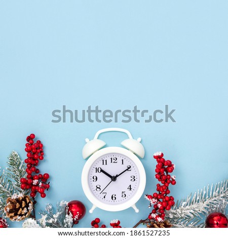 Winter composition of alarm clock, mistletoe, pine cones and fir branches on blue background. Christmas time concept. Top view, copy space