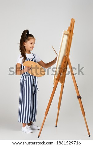 cute little girl holding a wooden art palette and brush on studio background. child painting. Full length