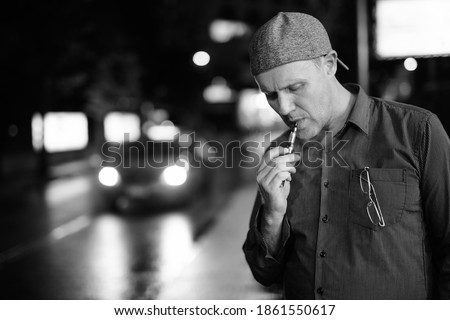 Mature man smoking electronic cigarette in the streets at night