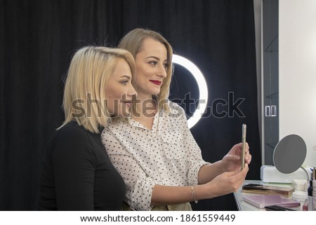Portrait of two female friends who take photos of themselves and their hairstyles in a hair salon.
