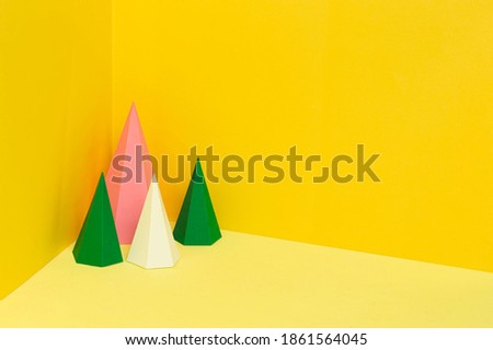 Multi-colored hexagonal paper pyramids stand in corner on yellow background. Paper art and craft
