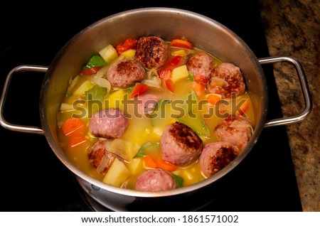 Pot with stew, meatballs, potatoes, carrots, green peppers being cooked on a ceramic stove.