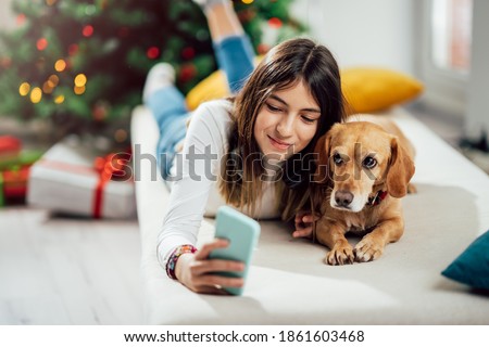 Teenage girl and her dog take a selfie in front of a Christmas tree.