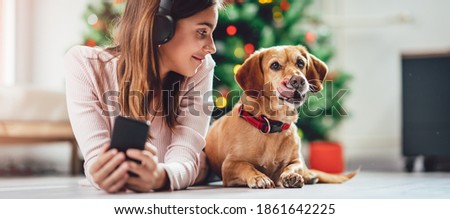 A teenage girl listens to music while lying on the floor with her dog near the Christmas tree