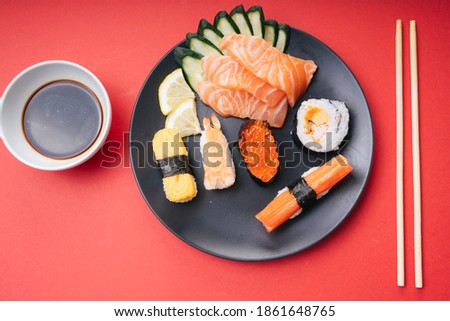 Japanese sushi and maki rolls with salmon sashimi on black plate with soy sauce and chopstick.