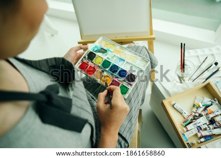 Professional female artist using colour palette painting on canvas.