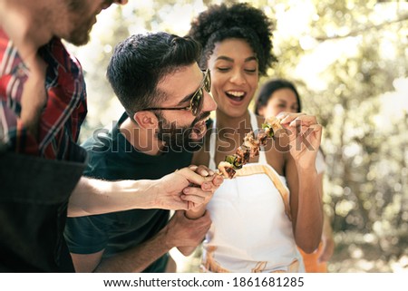Group of happy, multiracial, friends joking in the park eating skewers and having fun together. Togetherness, diversity and  friendship lifestyle concept.
