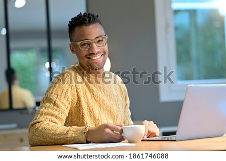 Portrait of cheerful ethnic guy working from home and having a coffee break Royalty-Free Stock Photo #1861746088