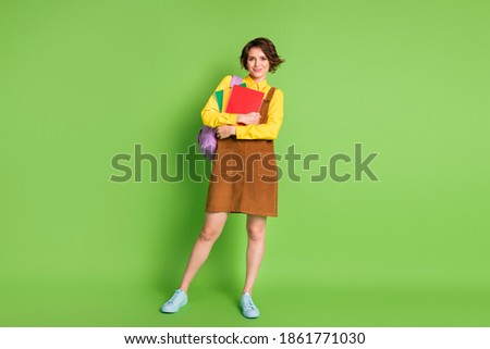Full size photo of pretty cute brunette girl stand hold copybooks rucksack wear brown dress sneakers isolated on green background