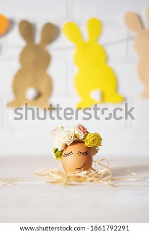 Easter egg with funny face. Funny easter egg decorated yellow roses wreath and paper bunnies. Easter egg is sleeping
