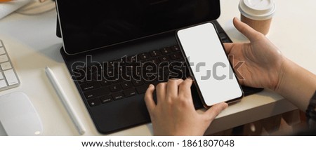 Top view of female hand holding smartphone on tablet keyboard in office room, clipping path