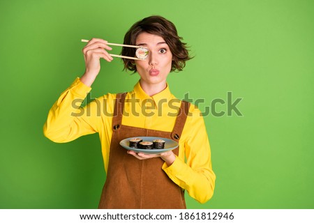 Photo of funny girl hold chopsticks plate sushi hide eye with roll pout lips wear yellow shirt overall isolated green color background
