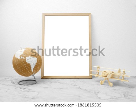 Blank frame on marble table with plane toy and globe.
